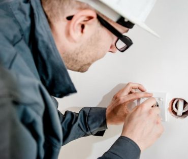 Electrician in a hard hat and safety glasses installing a wall outlet in a home